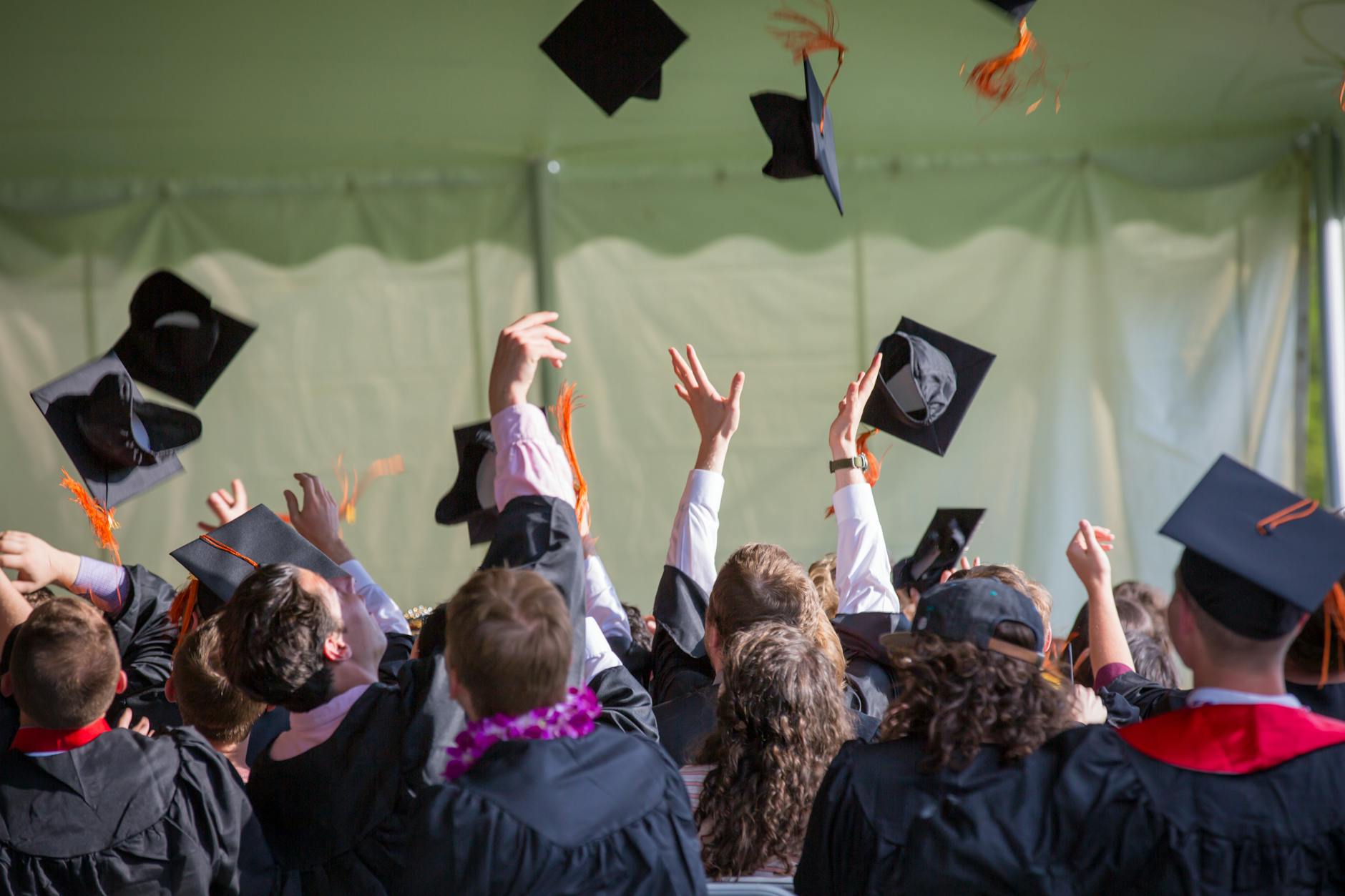 Multiple college students graduating from college and throwing their hats in the air with backs turned to the camera.
