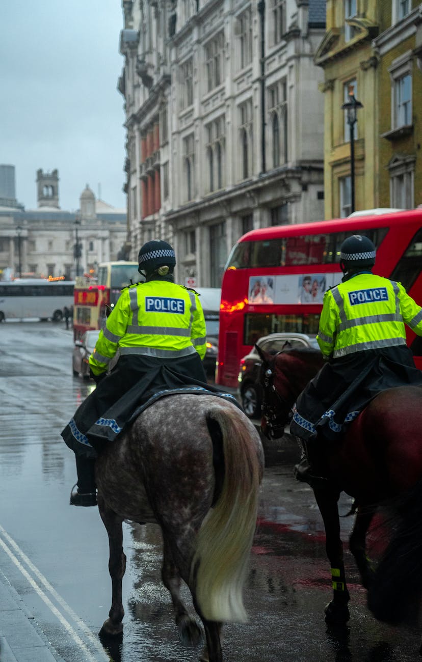 2 UK police officers on top of horses. A red bus in the background