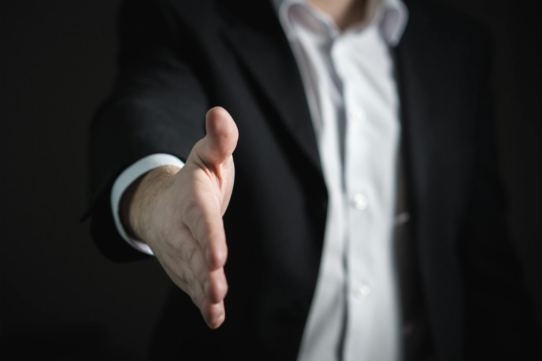 A business man in black tuxedo extending a hand shake.