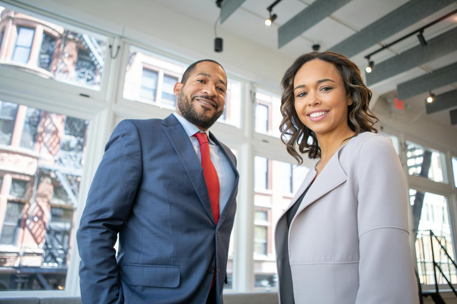 2 young professionals all smile after migrating to the UK. Photo shows a young man and woman all smiles as they pose for the camera.