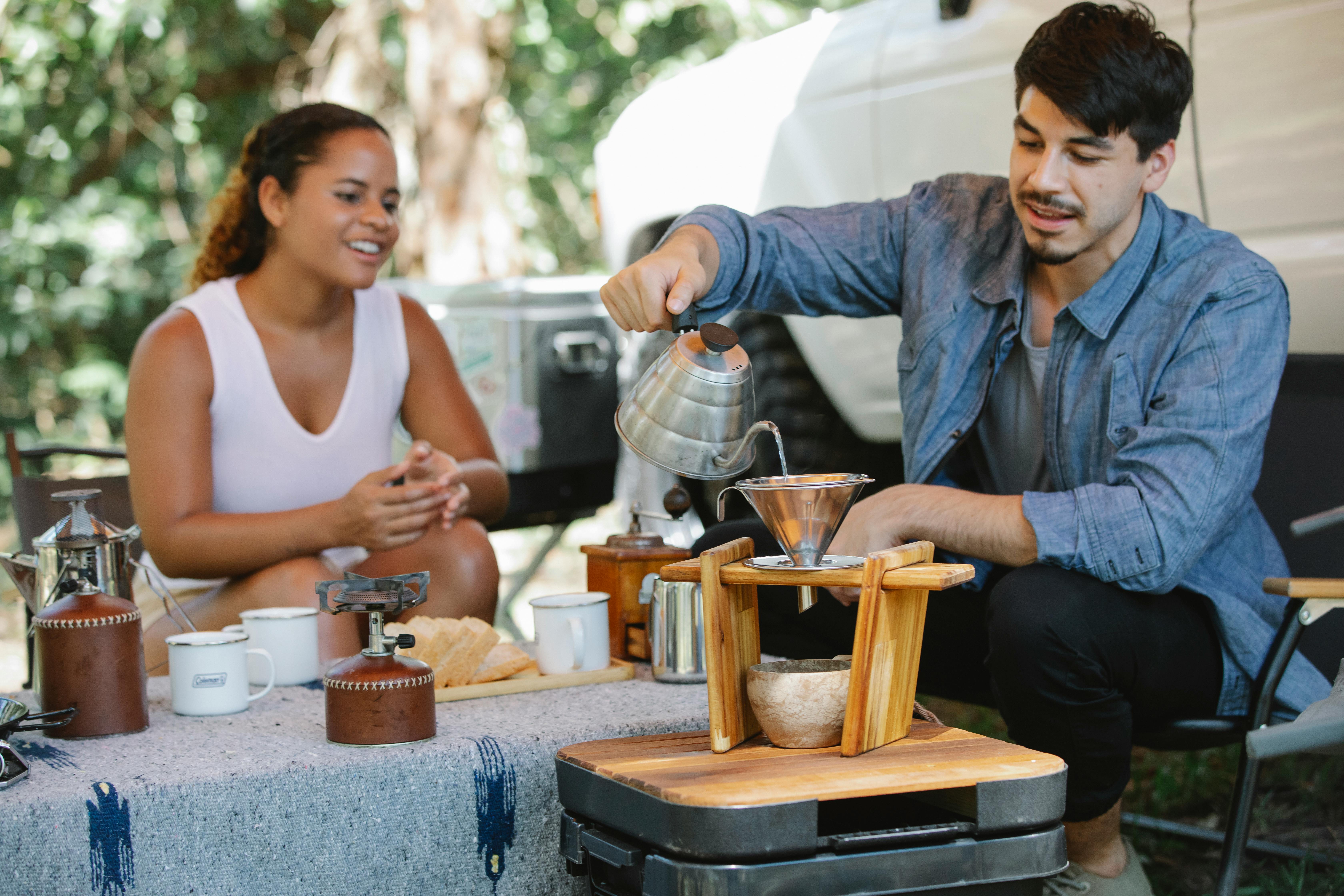 a man pouring his wife coffee outside their van